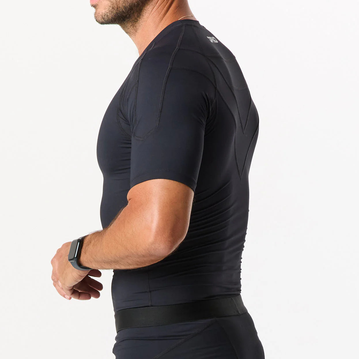 A person shown from the side against a white background wears a fitted black short-sleeve DFND Compression Short + Shirt Gym Kit and a black wristwatch.