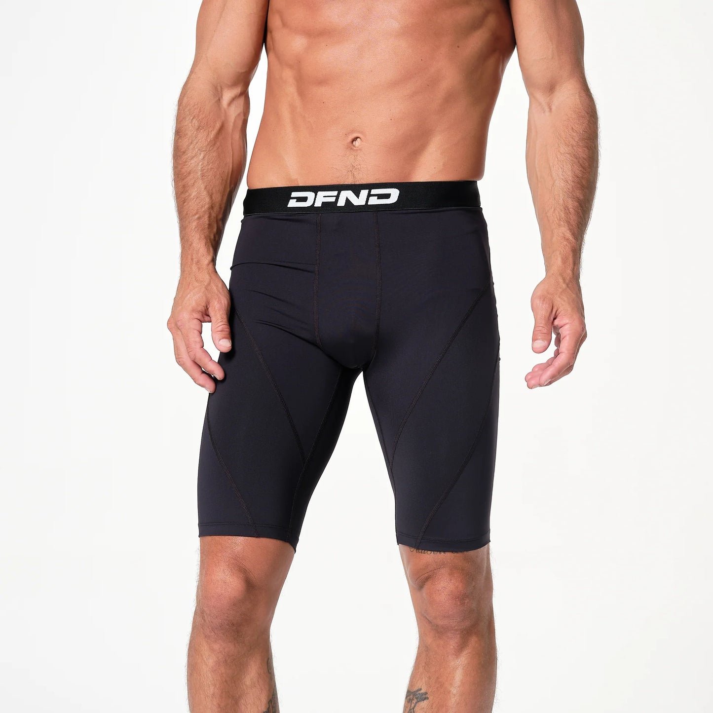 A person wearing the DFND Compression Short + Shirt Gym Kit, featuring black graduated compression shorts with a DFND logo waistband, stands against a plain white background.