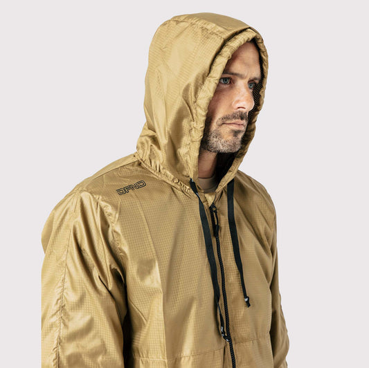 A man wearing a light brown DFND Storm Jkt with black drawstrings looks to the side against a plain background.