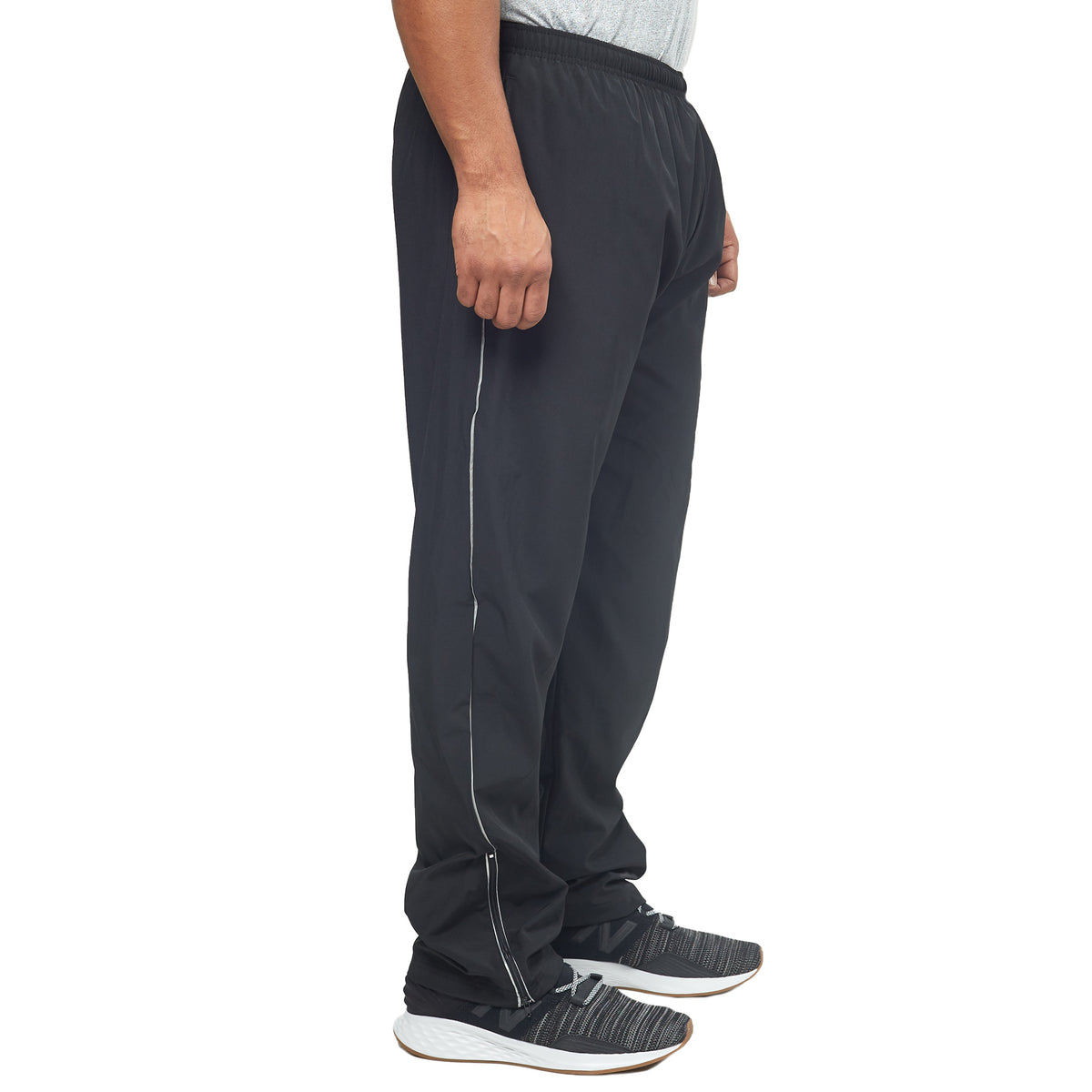 A person stands in profile wearing DFND FLASH TECH PANTS, crafted from Quick Dry fabric in black with a white stripe, paired with a gray shirt and black athletic shoes with white soles.